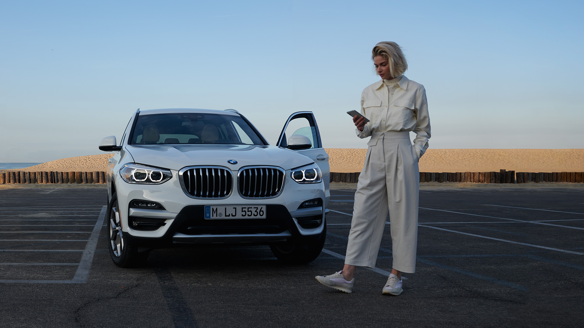 Жена ползва My BMW App на смартфона си Жена ползва My BMW App на BMW ConnectedDrive на смартфона си пред бяло BMW X5