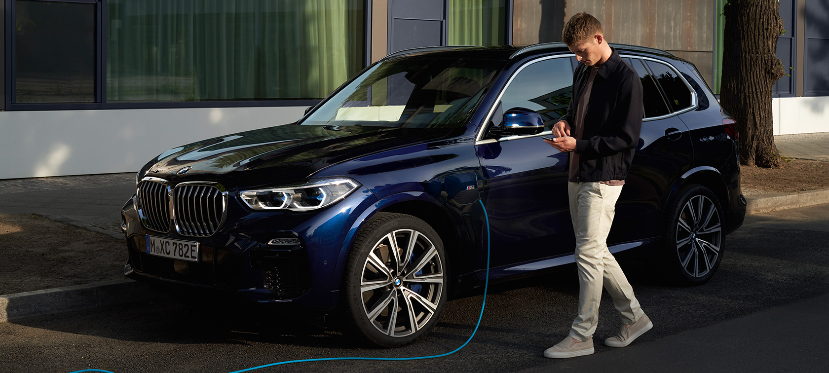 Мъж ползва My BMW App на смартфона си Мъж ползва My BMW App на BMW ConnectedDrive на смартфона, докато неговото BMW X5 Plug-in хибрид се зарежда.