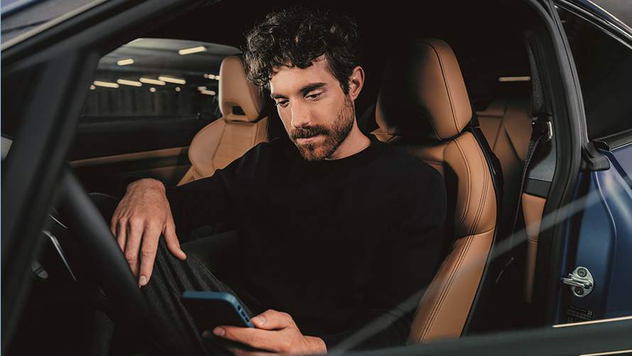 Мъж седи в BMW Мъж седи в BMW и гледа смартфона си