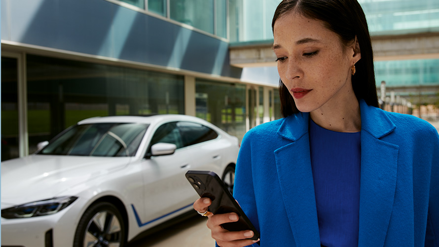 Жена стои пред BMW Жена стои пред BMW и гледа смартфона си