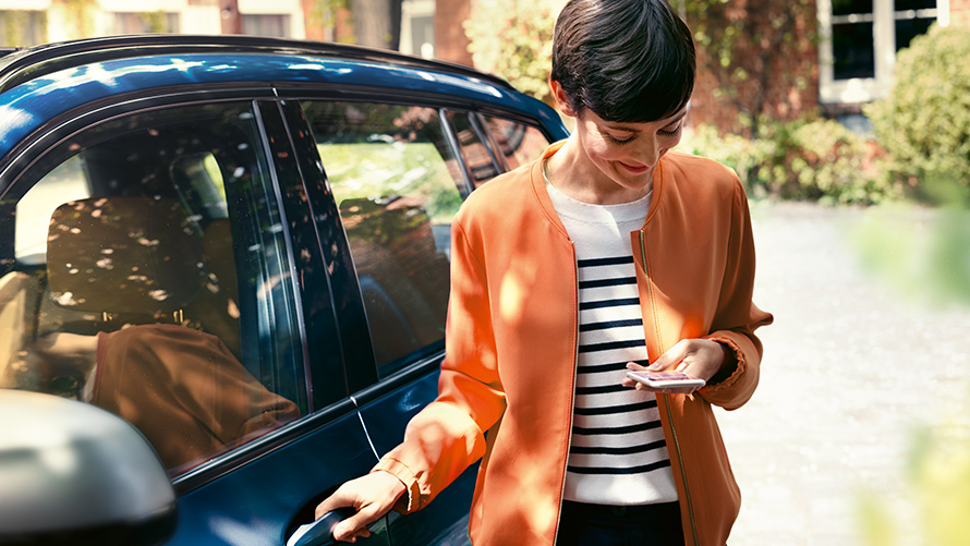 BMW Телеуслуги. Жена със смартфон стои до вратата на своето BMW