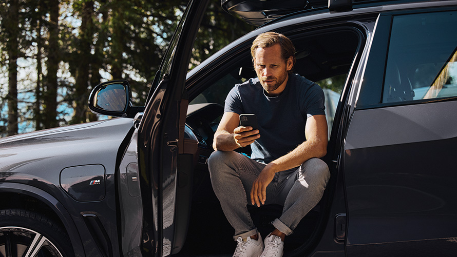 Мъж седи в BMW и гледа смартфона си BMW Аксесоари за пролетта и лятото мъж седи в BMW и гледа смартфона си