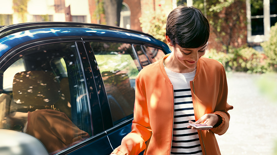BMW летни оферти BMW Телеуслуги BMW летни оферти BMW Телеуслуги, жена стои пред BMW и използва смартфон