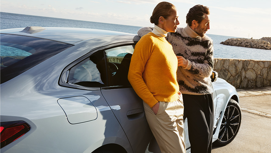 BMW Service Inclusive Продължителност и срокове за нови автомобили BMW Service Inclusive мъж и жена се облягат на BMW i4 на брега