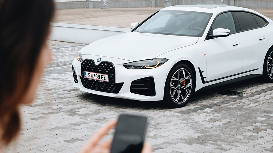 Жена използва своя смартфон. Фокусирайте се върху BMW i4. Жена използва своя смартфон. Фокусирайте се върху BMW i4.