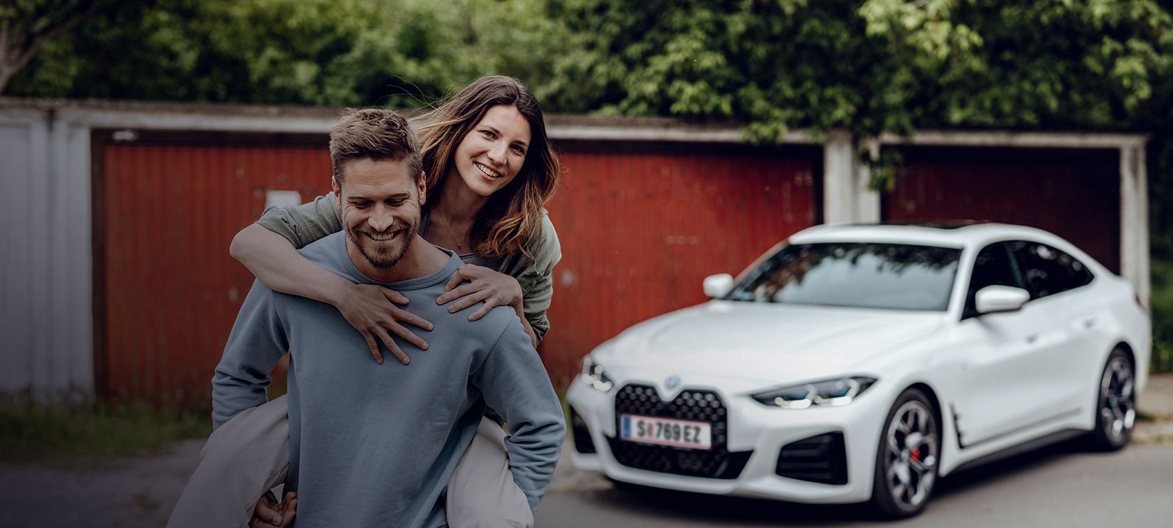 Усмихнат мъж, който се отдалечава от BMW i4, носейки усмихната жена на гърба си. Усмихнат мъж, който се отдалечава от BMW i4, носейки усмихната жена на гърба си.