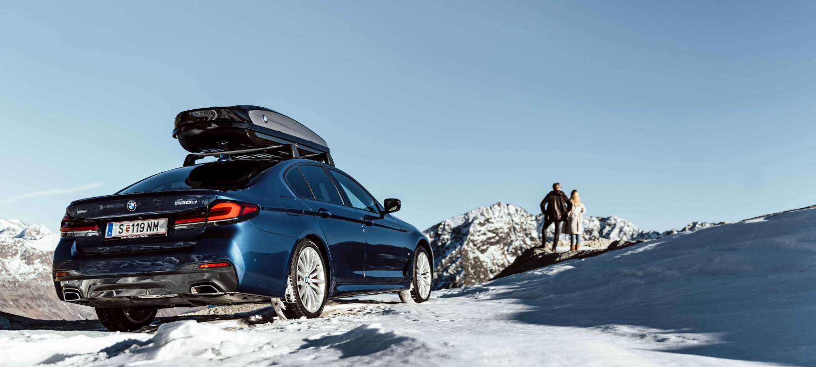 Оригинални BMW Аксесоари и BMW Service за есента и зимата. Жена и мъж седят се смеят на шейна в снега
