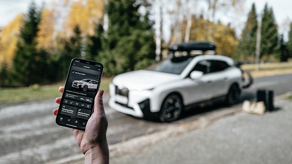 Телефон с отворен My BMW App и iX с аксесоари на заден план. Телефон с отворен My BMW App и iX с аксесоари на заден план.